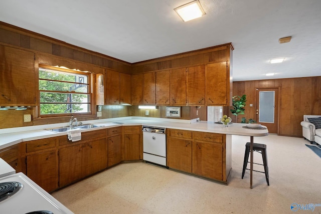 kitchen with white dishwasher, a peninsula, a breakfast bar, light countertops, and light floors