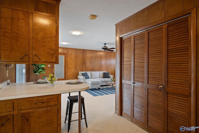 kitchen featuring ceiling fan, wood walls, open floor plan, light countertops, and brown cabinets