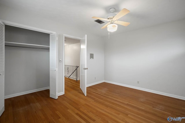 unfurnished bedroom with wood finished floors, a ceiling fan, visible vents, baseboards, and a closet