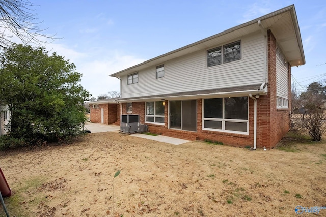 rear view of property with central AC, brick siding, a lawn, and a patio area