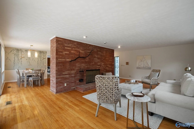 living room featuring a textured ceiling, visible vents, baseboards, a brick fireplace, and light wood finished floors