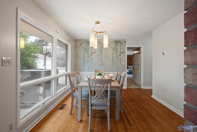 dining area featuring an accent wall, visible vents, baseboards, and wood finished floors