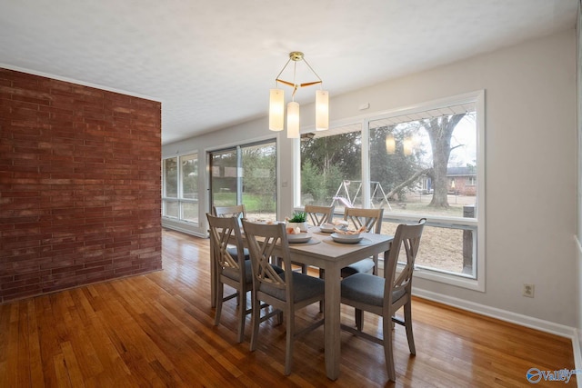 dining area with brick wall, wood finished floors, and baseboards