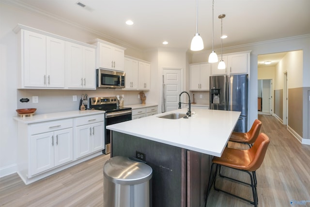 kitchen featuring pendant lighting, white cabinets, stainless steel appliances, sink, and a kitchen island with sink