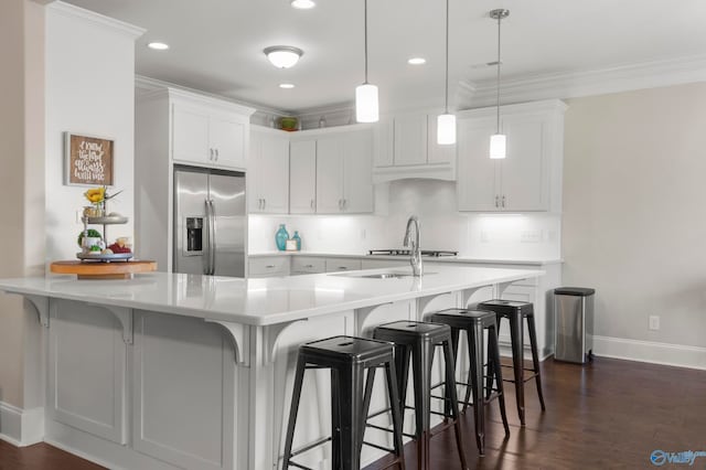 kitchen with a breakfast bar, pendant lighting, stainless steel fridge, and white cabinets