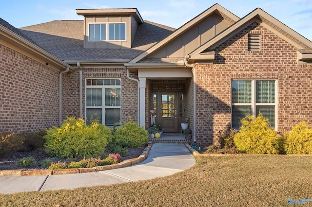 property entrance with brick siding, roof with shingles, and a lawn