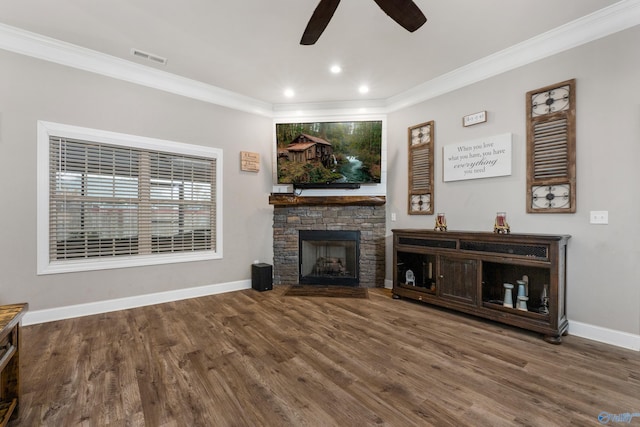 living room with hardwood / wood-style floors, ceiling fan, a stone fireplace, and crown molding