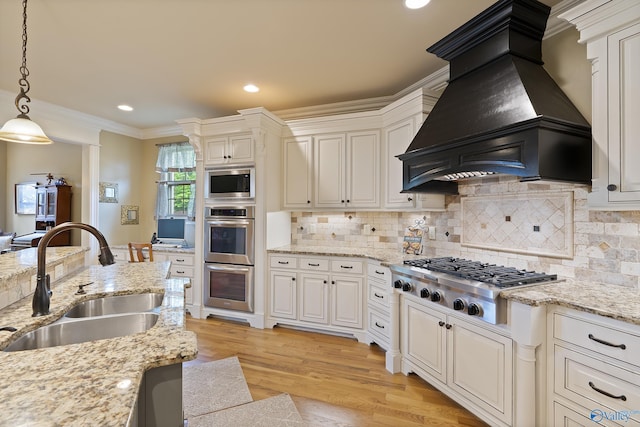 kitchen with pendant lighting, premium range hood, light wood-type flooring, a sink, and stainless steel appliances
