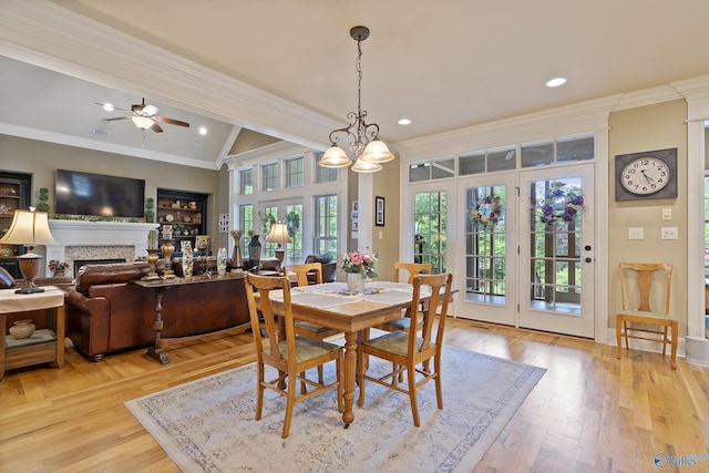 dining space with a fireplace, ornamental molding, ceiling fan with notable chandelier, vaulted ceiling with beams, and light wood-style flooring