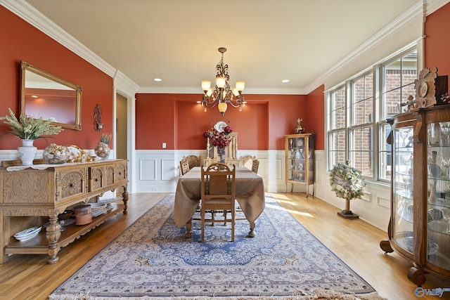 dining room with an inviting chandelier, ornamental molding, wood finished floors, and a wainscoted wall