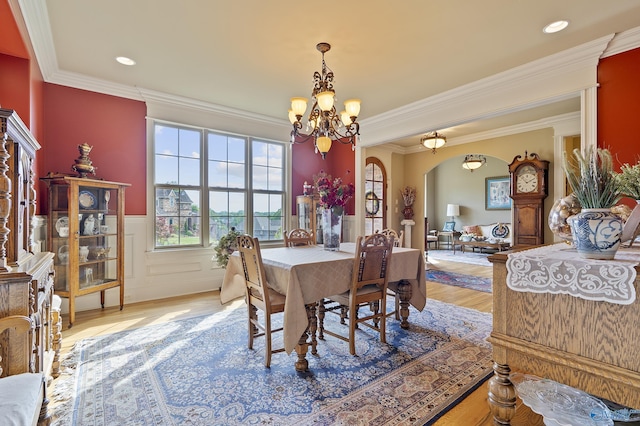 dining area featuring crown molding, arched walkways, a wainscoted wall, a chandelier, and light wood-style flooring