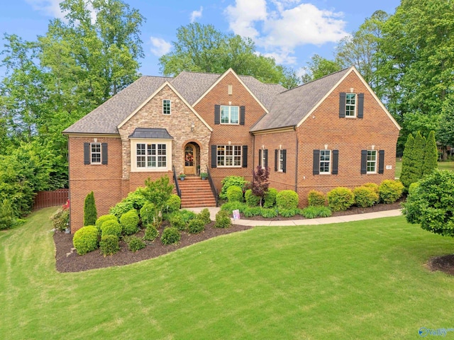 view of front facade featuring brick siding, a front lawn, roof with shingles, and fence