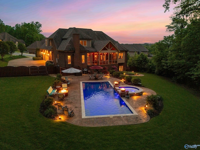 back of house at dusk featuring a pool with connected hot tub, fence private yard, a lawn, a patio, and a fire pit