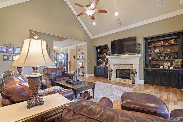 living area featuring a ceiling fan, a fireplace with flush hearth, high vaulted ceiling, light wood-style floors, and ornamental molding