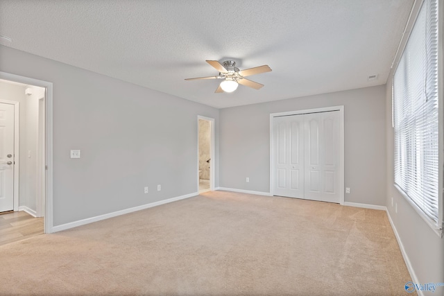 unfurnished bedroom featuring a textured ceiling, a closet, light colored carpet, and ceiling fan