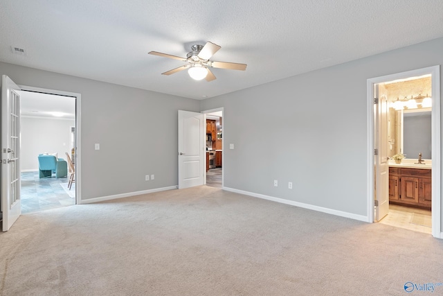 unfurnished bedroom featuring a textured ceiling, ensuite bathroom, ceiling fan, and light carpet