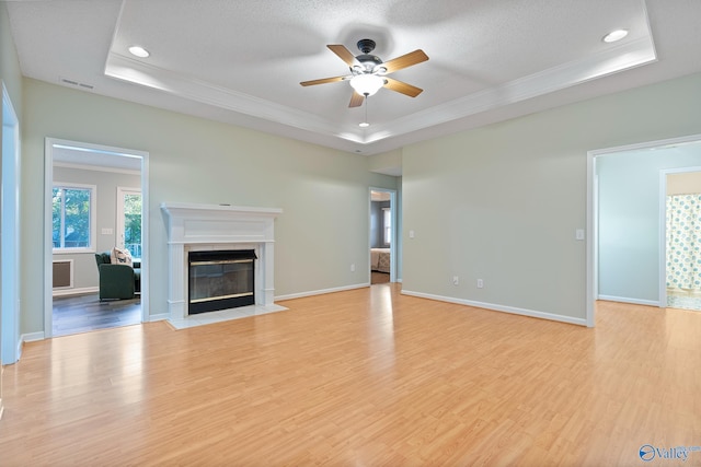 unfurnished living room featuring a tile fireplace, ceiling fan, a raised ceiling, a textured ceiling, and light wood-type flooring