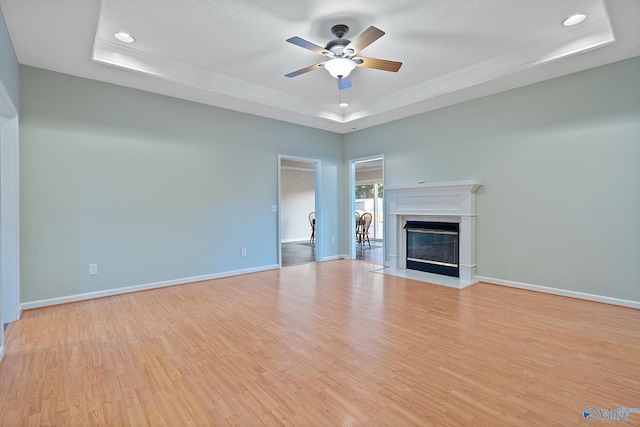 unfurnished living room with a tray ceiling, ceiling fan, and light wood-type flooring