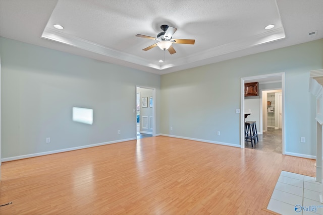 empty room with light wood-type flooring, a textured ceiling, and a tray ceiling