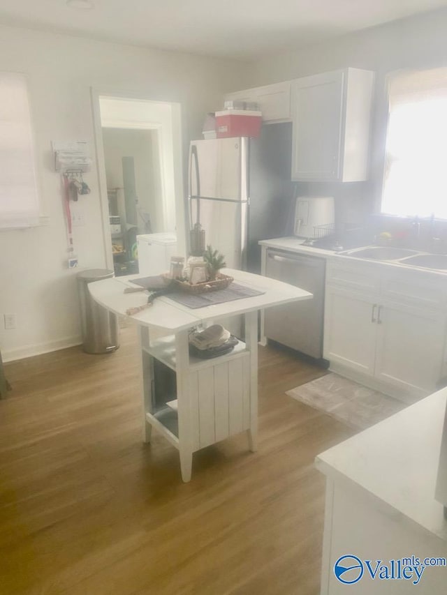 kitchen featuring light wood-style floors, white cabinetry, stainless steel dishwasher, and freestanding refrigerator