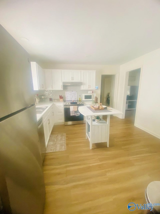 kitchen featuring light wood finished floors, under cabinet range hood, stainless steel appliances, and light countertops