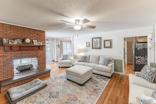 living room with ceiling fan, a fireplace, a textured ceiling, and light wood-type flooring