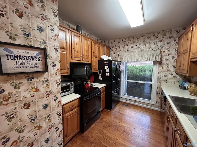 kitchen with sink, light hardwood / wood-style flooring, and black appliances