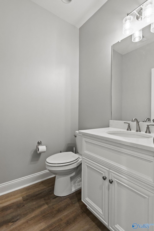 half bathroom with toilet, wood finished floors, vanity, and baseboards