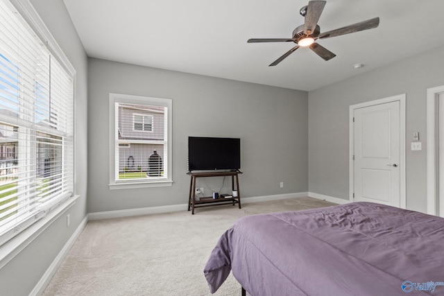 bedroom featuring light colored carpet, multiple windows, baseboards, and a ceiling fan