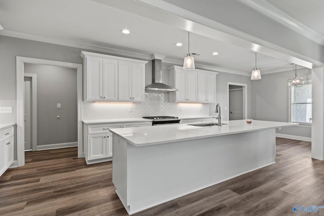 kitchen featuring wall chimney range hood, a sink, white cabinets, ornamental molding, and a center island with sink