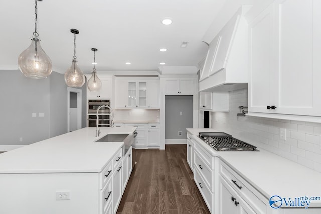 kitchen with appliances with stainless steel finishes, pendant lighting, white cabinetry, an island with sink, and sink