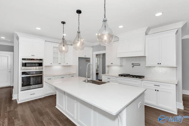 kitchen featuring appliances with stainless steel finishes, white cabinetry, sink, hanging light fixtures, and a kitchen island with sink