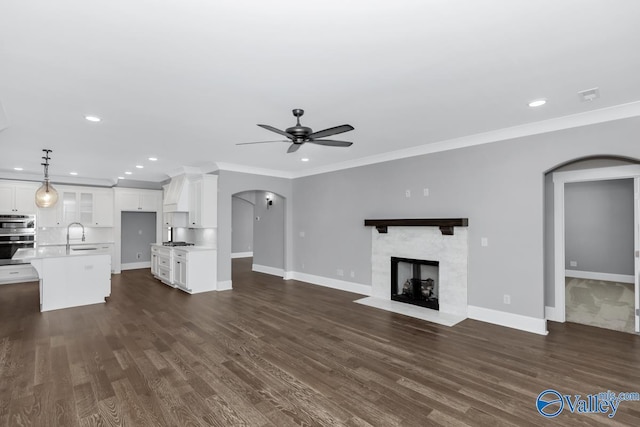 unfurnished living room featuring sink, crown molding, a tile fireplace, and ceiling fan