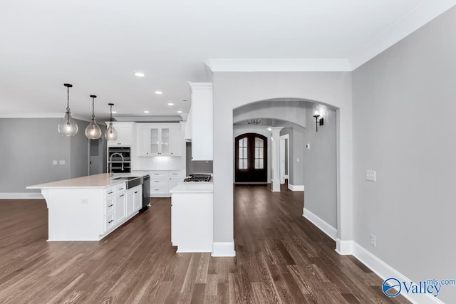 kitchen with ornamental molding, a center island with sink, white cabinets, and decorative light fixtures