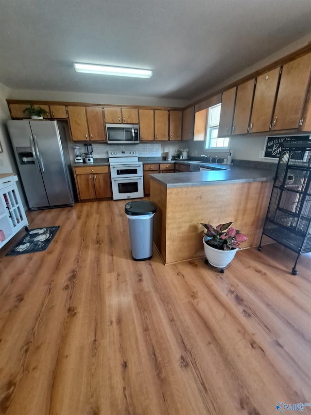 kitchen with stainless steel appliances, sink, light hardwood / wood-style floors, and kitchen peninsula