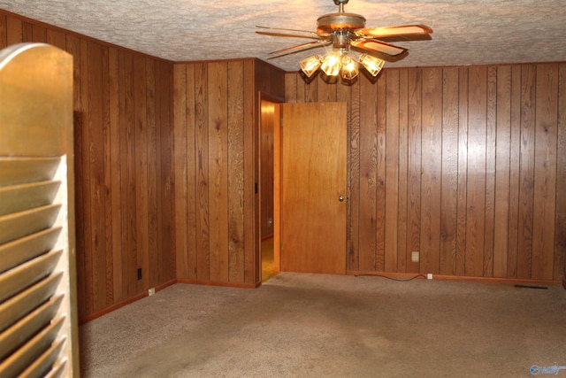 empty room with ceiling fan, a textured ceiling, wood walls, and carpet flooring