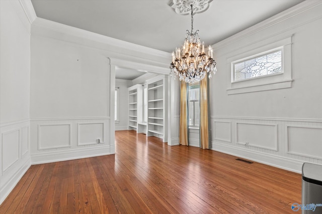 unfurnished dining area featuring a chandelier, hardwood / wood-style floors, crown molding, and built in features