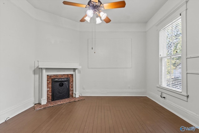 unfurnished living room featuring ceiling fan, a fireplace, dark hardwood / wood-style floors, and a healthy amount of sunlight