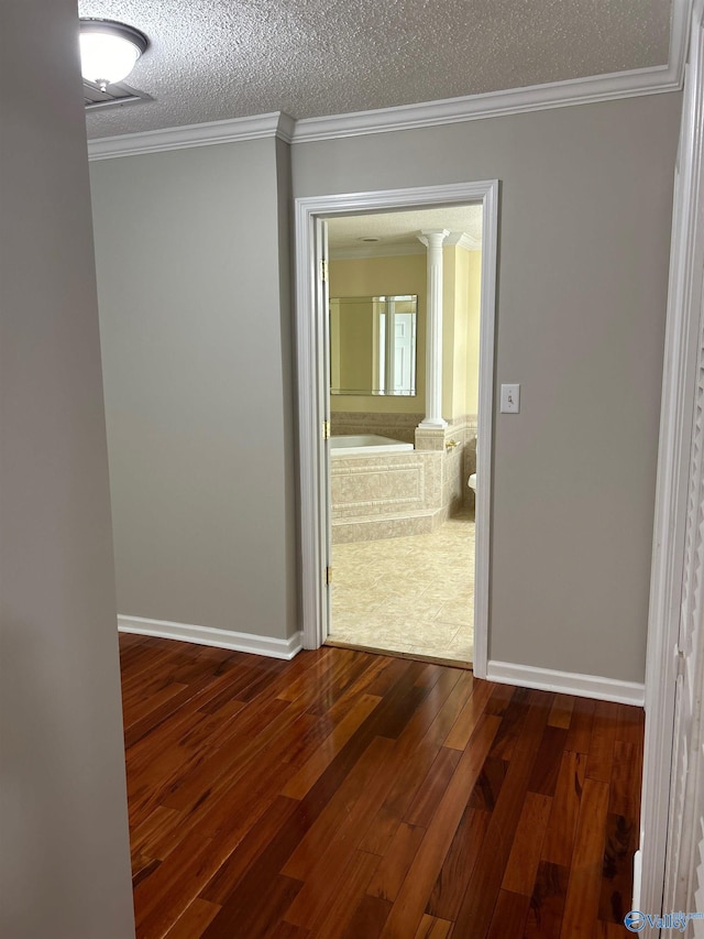 hallway with dark hardwood / wood-style flooring, ornamental molding, a textured ceiling, and ornate columns