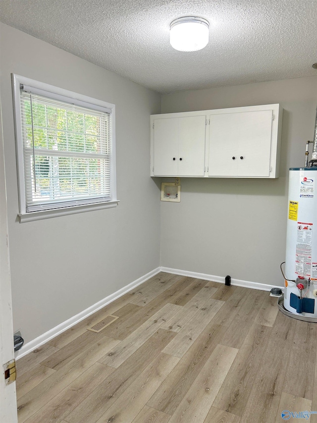 laundry area featuring gas water heater, cabinets, washer hookup, light hardwood / wood-style floors, and a textured ceiling