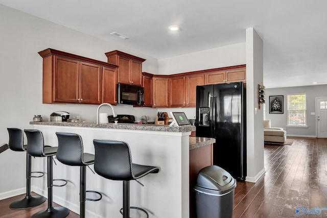 kitchen with dark hardwood / wood-style floors, kitchen peninsula, a breakfast bar area, and black appliances