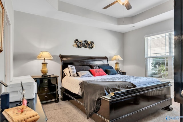 carpeted bedroom with a raised ceiling and ceiling fan