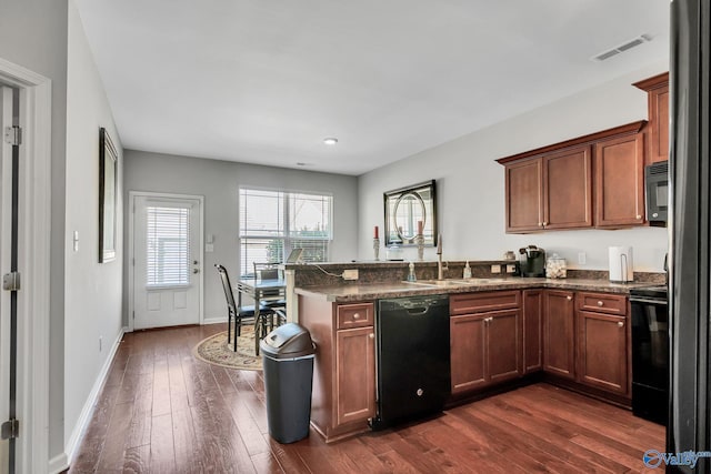 kitchen with black appliances, sink, dark stone countertops, dark hardwood / wood-style flooring, and kitchen peninsula