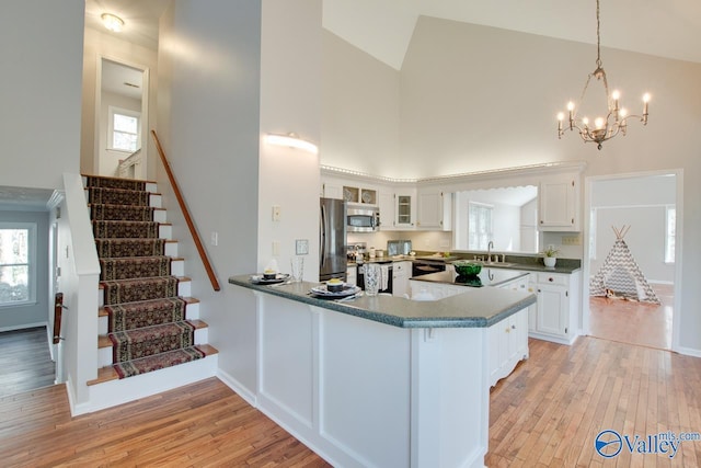 kitchen featuring appliances with stainless steel finishes, white cabinetry, decorative light fixtures, high vaulted ceiling, and kitchen peninsula