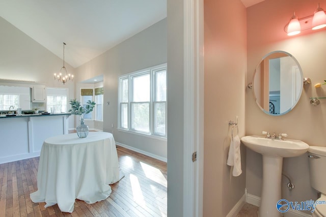 bathroom featuring lofted ceiling, wood-type flooring, sink, toilet, and a chandelier