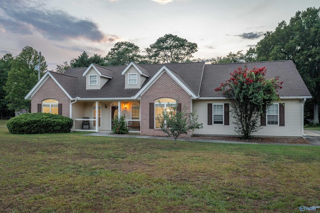 cape cod house featuring a lawn and covered porch