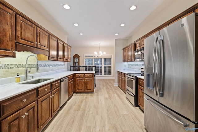 kitchen with sink, light hardwood / wood-style flooring, kitchen peninsula, pendant lighting, and stainless steel appliances