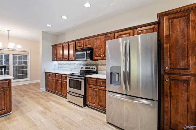 kitchen with a chandelier, hanging light fixtures, stainless steel appliances, light hardwood / wood-style flooring, and backsplash