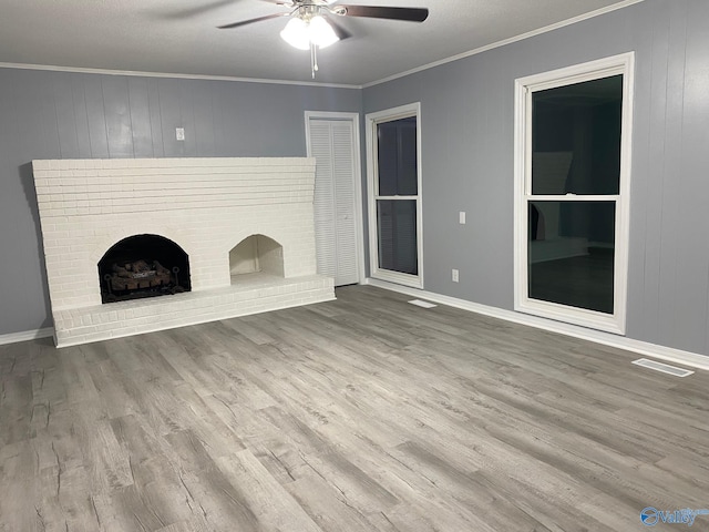 unfurnished living room featuring a textured ceiling, hardwood / wood-style flooring, ceiling fan, crown molding, and a fireplace