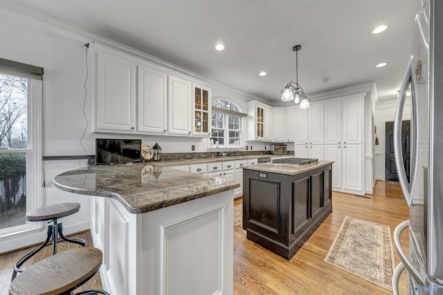 kitchen featuring decorative light fixtures, white cabinets, dark stone counters, a center island, and stainless steel appliances